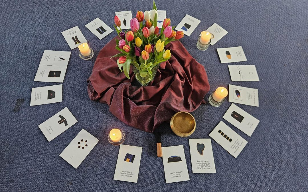 Ein Bodenarrangement aus Blumen, Kerzen und Postkarten mit den Wir-Prozess Kommunkationsempfehlungen auf blauem Teppich